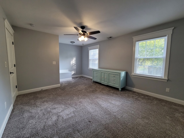 empty room featuring ceiling fan, a healthy amount of sunlight, and dark colored carpet