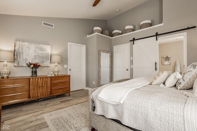 bedroom featuring ceiling fan, a barn door, visible vents, and wood finished floors