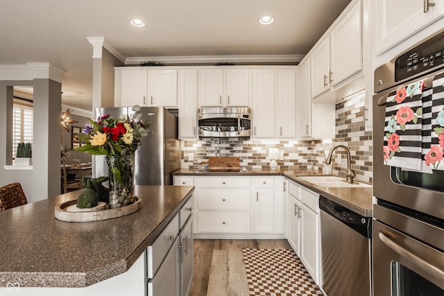 kitchen with dark countertops, a sink, appliances with stainless steel finishes, white cabinetry, and crown molding