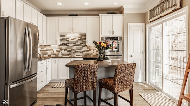 kitchen with a breakfast bar area, light wood-style flooring, a sink, appliances with stainless steel finishes, and crown molding