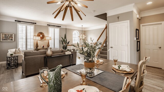 dining area with light wood finished floors, crown molding, baseboards, stairway, and ceiling fan with notable chandelier