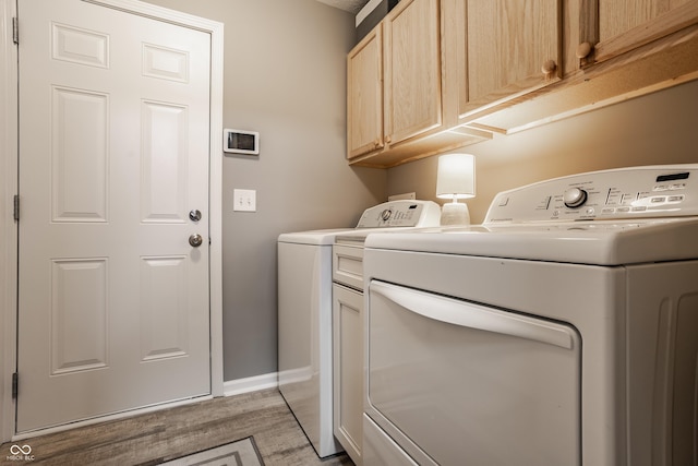 clothes washing area featuring light wood-style flooring, cabinet space, independent washer and dryer, and baseboards