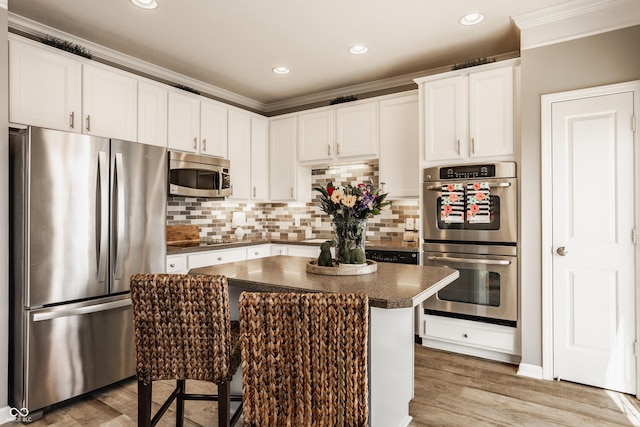 kitchen with dark countertops, a center island, appliances with stainless steel finishes, light wood finished floors, and decorative backsplash