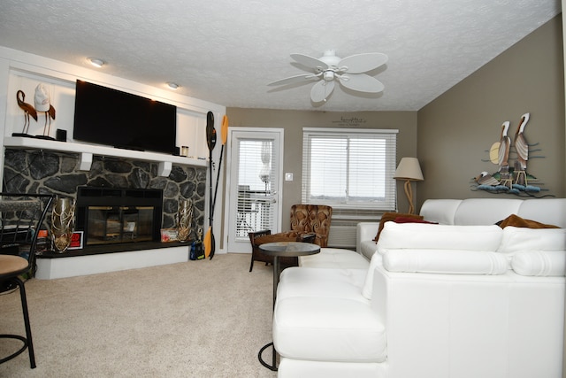 carpeted living room featuring a stone fireplace, a textured ceiling, and ceiling fan