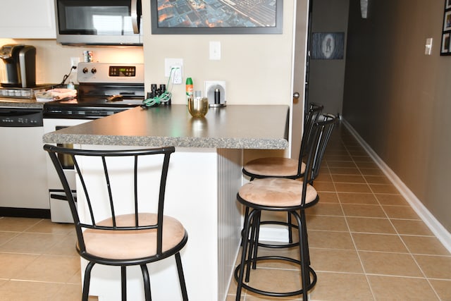 kitchen featuring a kitchen bar, appliances with stainless steel finishes, tile patterned floors, and white cabinetry