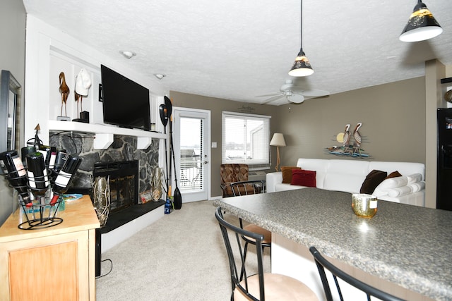 carpeted dining area featuring a stone fireplace, a textured ceiling, and ceiling fan