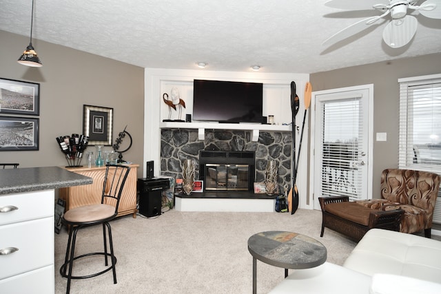 living room with a stone fireplace, a textured ceiling, carpet, and ceiling fan