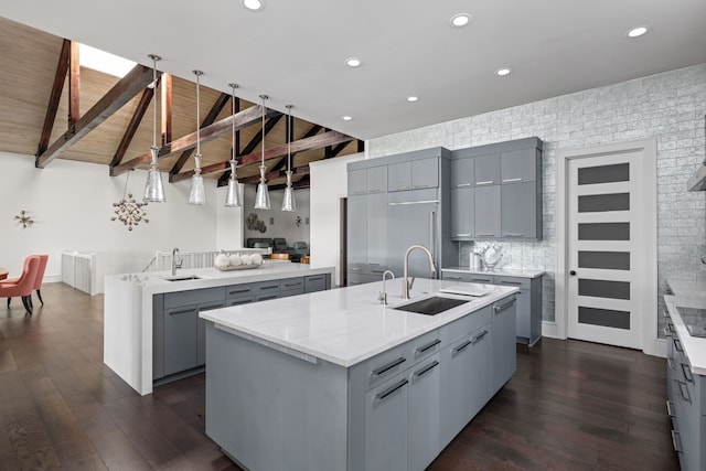 kitchen featuring dark wood-type flooring, a center island with sink, gray cabinets, and a sink