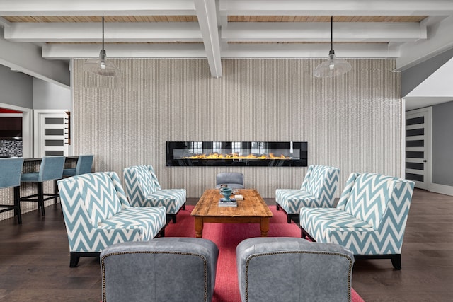 living area with an accent wall, wood finished floors, beamed ceiling, and a glass covered fireplace