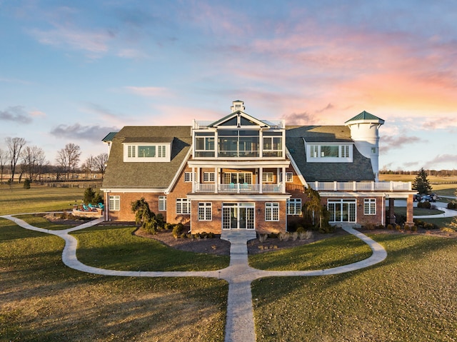 rear view of property featuring brick siding, a yard, french doors, and a balcony