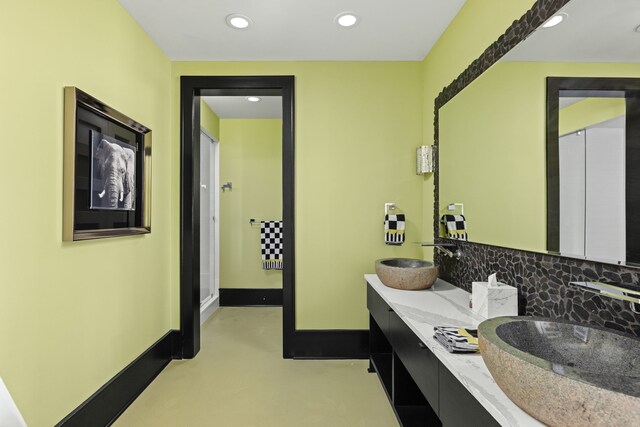 bathroom with baseboards, backsplash, a sink, and recessed lighting