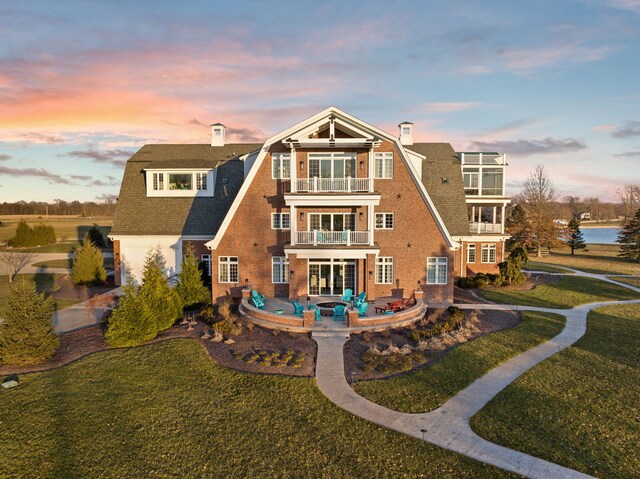 back of property at dusk with a balcony, a patio area, a chimney, and brick siding