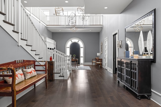 entryway featuring arched walkways, a towering ceiling, baseboards, stairway, and hardwood / wood-style floors