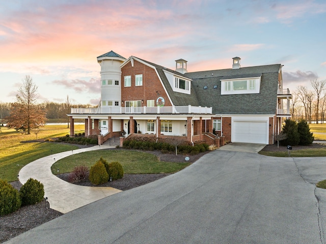 view of front of house with concrete driveway, a gambrel roof, roof with shingles, a front lawn, and brick siding