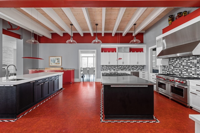 kitchen featuring range with two ovens, beam ceiling, a sink, and an island with sink