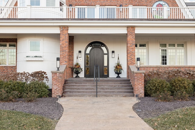 view of exterior entry with a balcony and brick siding