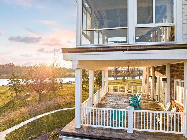 patio terrace at dusk featuring a water view and covered porch