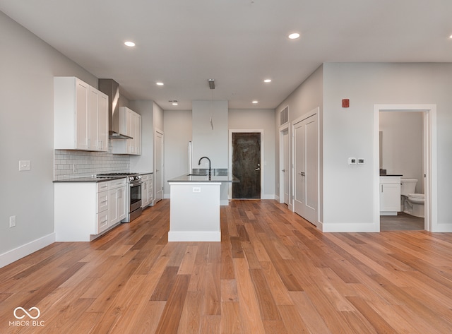 kitchen with white cabinetry, light hardwood / wood-style flooring, stainless steel stove, and a kitchen island with sink