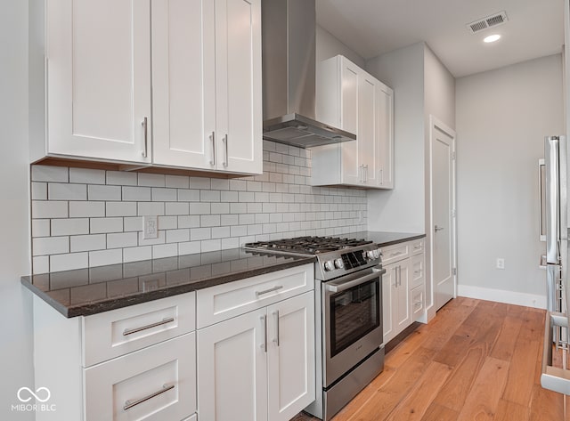 kitchen featuring dark stone counters, high end stainless steel range oven, wall chimney exhaust hood, light hardwood / wood-style floors, and white cabinetry