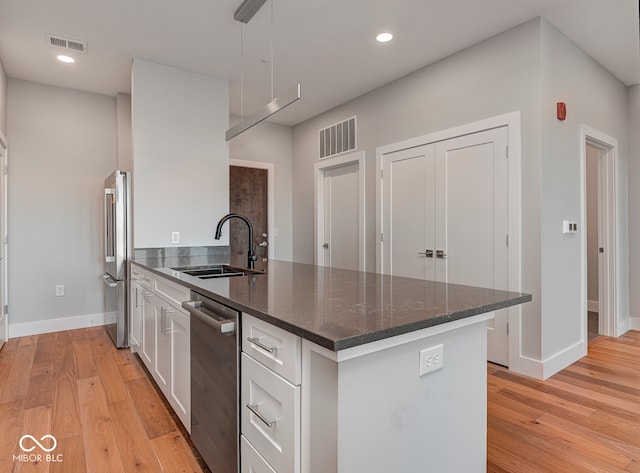 kitchen with sink, stainless steel appliances, light hardwood / wood-style flooring, dark stone counters, and white cabinets