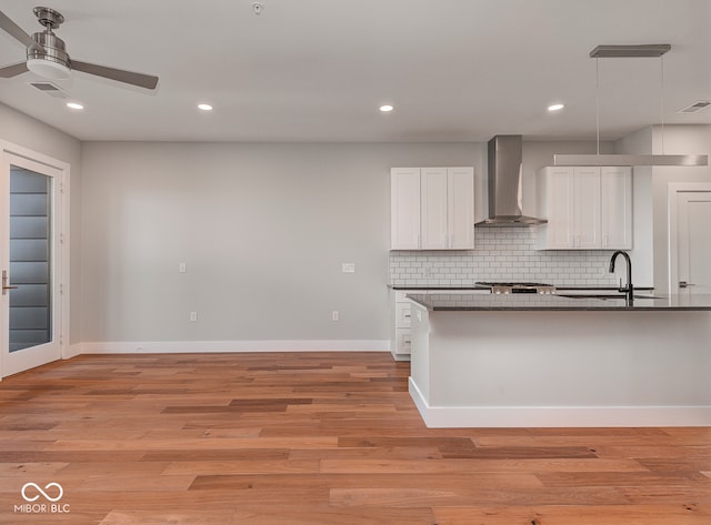 kitchen featuring backsplash, light hardwood / wood-style floors, white cabinetry, and wall chimney range hood