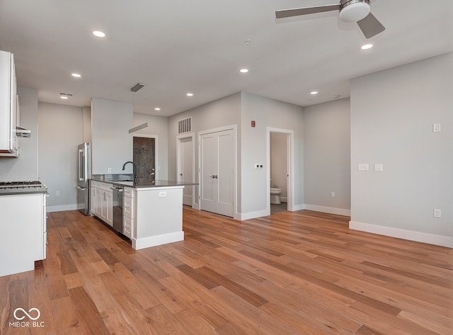 kitchen featuring sink, light wood-type flooring, an island with sink, appliances with stainless steel finishes, and white cabinetry