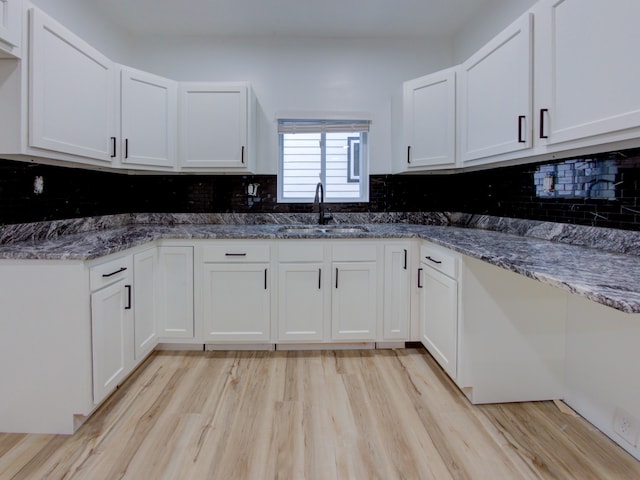 kitchen featuring white cabinets, light wood-type flooring, decorative backsplash, and sink