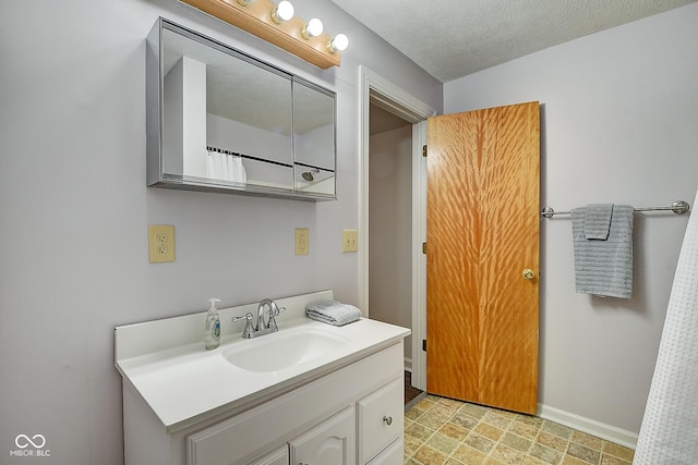 bathroom featuring a textured ceiling, stone finish flooring, vanity, and baseboards