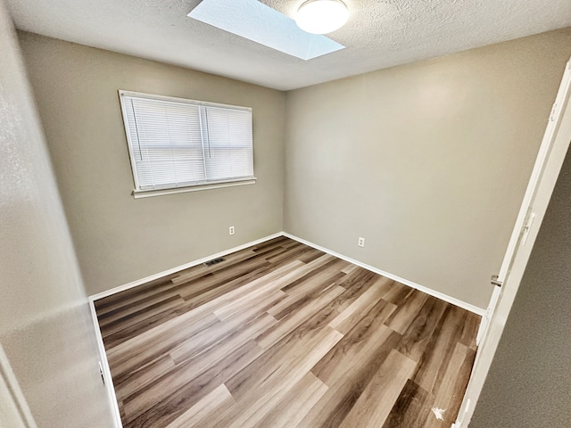 empty room featuring a skylight, hardwood / wood-style flooring, and a textured ceiling