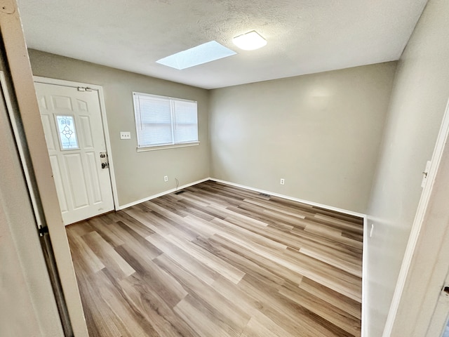 interior space with a skylight, a textured ceiling, and light hardwood / wood-style flooring