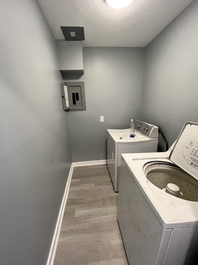 washroom with a textured ceiling, separate washer and dryer, electric panel, and light hardwood / wood-style flooring