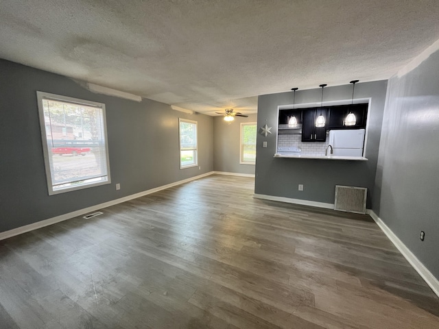 unfurnished living room featuring plenty of natural light, a textured ceiling, ceiling fan, and dark hardwood / wood-style floors