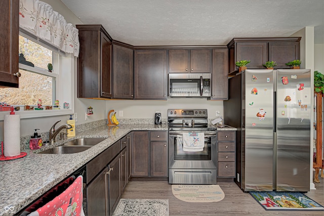 kitchen with light stone countertops, light wood-type flooring, dark brown cabinetry, stainless steel appliances, and sink