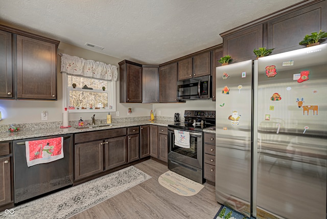 kitchen with light stone countertops, a textured ceiling, dark brown cabinets, light hardwood / wood-style floors, and stainless steel appliances