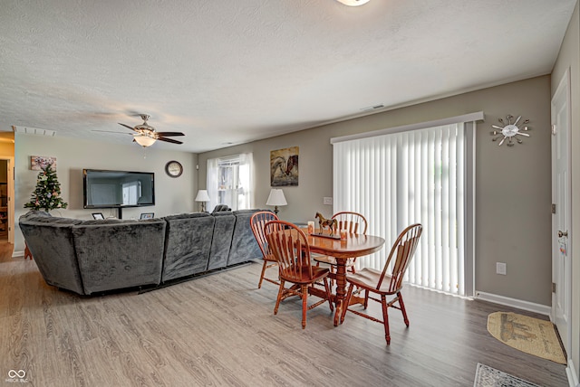 dining space with a textured ceiling, light wood-type flooring, and ceiling fan