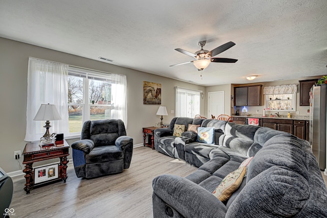 living room with ceiling fan, a textured ceiling, and light wood-type flooring