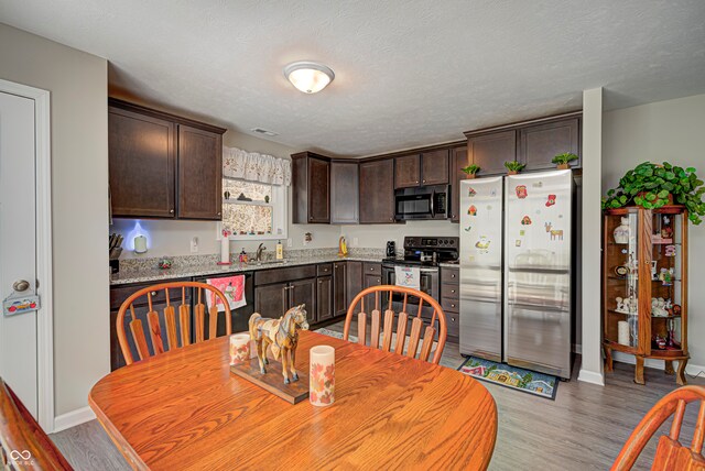 kitchen featuring appliances with stainless steel finishes, dark brown cabinetry, a textured ceiling, sink, and light hardwood / wood-style flooring