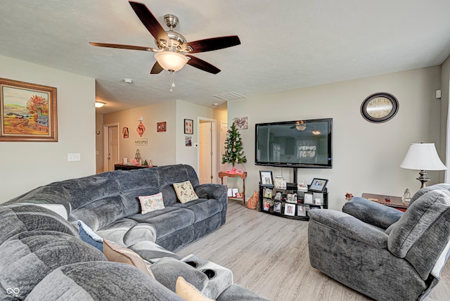 living room with ceiling fan, a textured ceiling, and light wood-type flooring