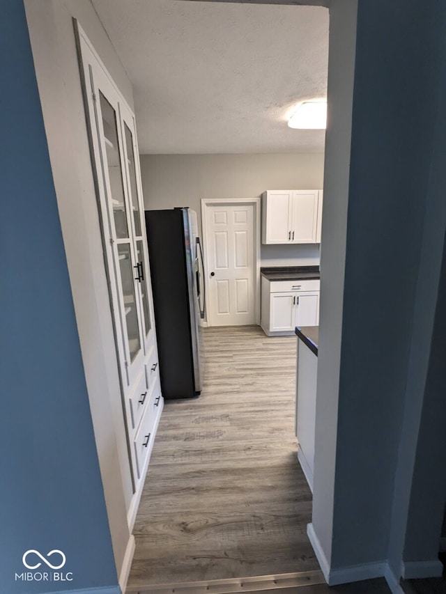 kitchen with white cabinets, light wood-type flooring, and stainless steel fridge