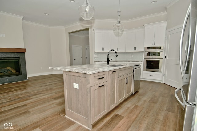 kitchen featuring sink, appliances with stainless steel finishes, decorative light fixtures, an island with sink, and light wood-type flooring