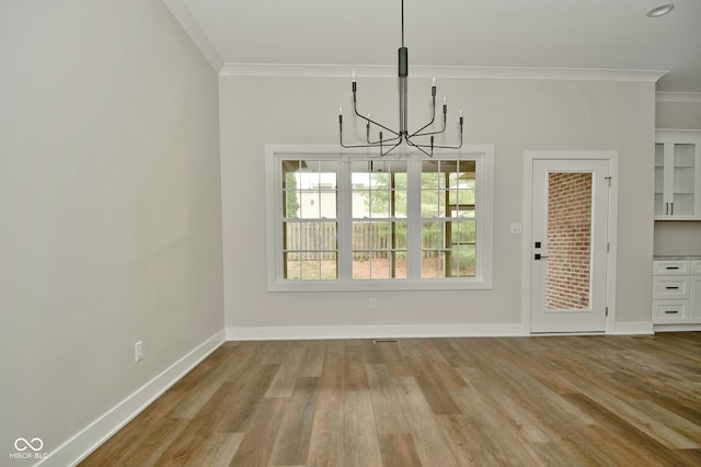 unfurnished dining area with a notable chandelier, light wood-type flooring, and ornamental molding