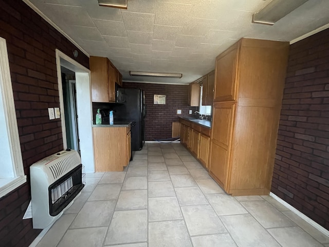 kitchen with sink, light tile patterned flooring, black appliances, brick wall, and heating unit