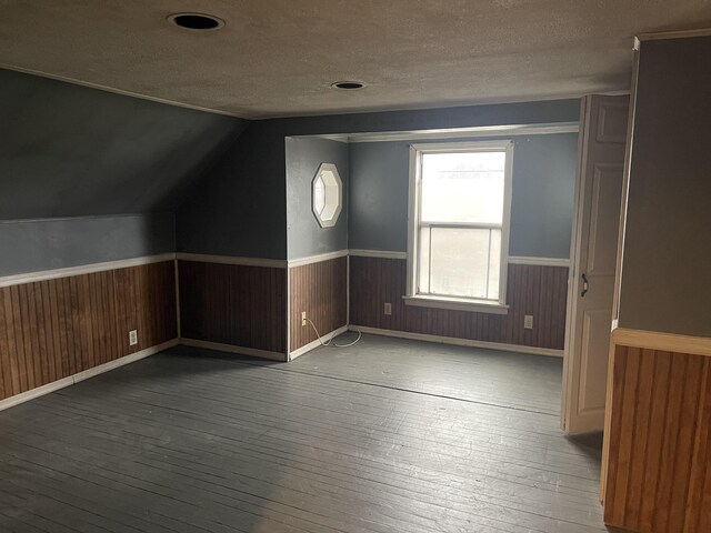 additional living space with vaulted ceiling, dark hardwood / wood-style flooring, and a textured ceiling