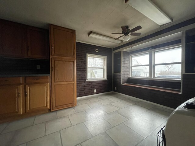 kitchen with light tile patterned flooring, ornamental molding, brick wall, and ceiling fan