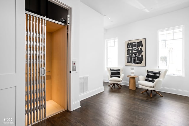 sitting room with a healthy amount of sunlight, elevator, and dark hardwood / wood-style flooring