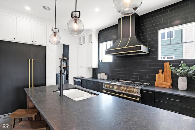 kitchen with decorative light fixtures, white cabinetry, premium appliances, wall chimney range hood, and a center island with sink