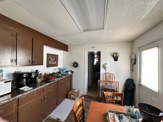 kitchen with hardwood / wood-style flooring, white microwave, a paneled ceiling, dark brown cabinetry, and sink