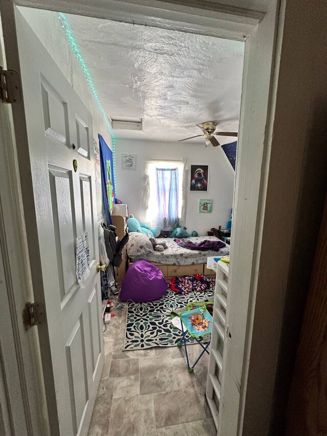 bedroom featuring ceiling fan, light tile floors, and a textured ceiling