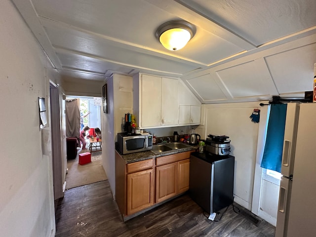 kitchen featuring dark wood-type flooring, dark stone countertops, vaulted ceiling, sink, and white refrigerator