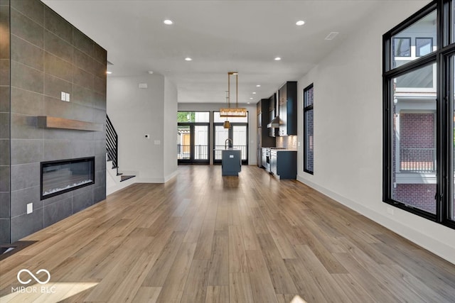 unfurnished living room featuring a tiled fireplace, hardwood / wood-style flooring, and a notable chandelier